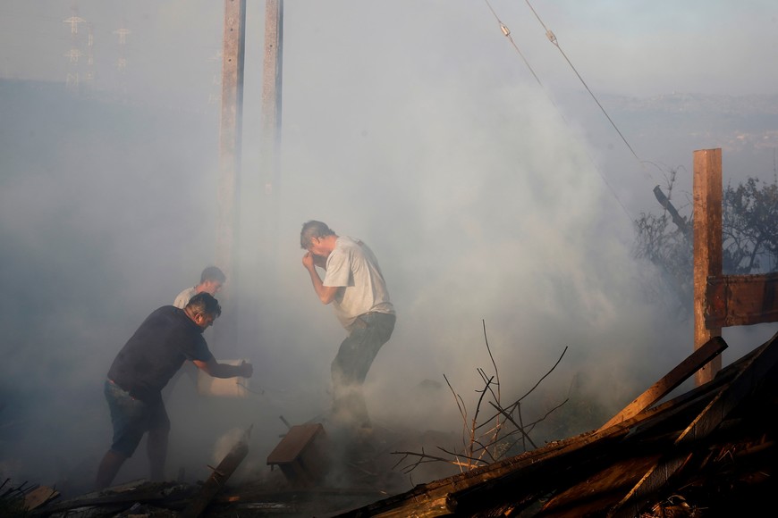 A man pours water over the remains of a burned house during a wildfire in Vina del Mar, Chile December 22, 2022. REUTERS/Rodrigo Garrido