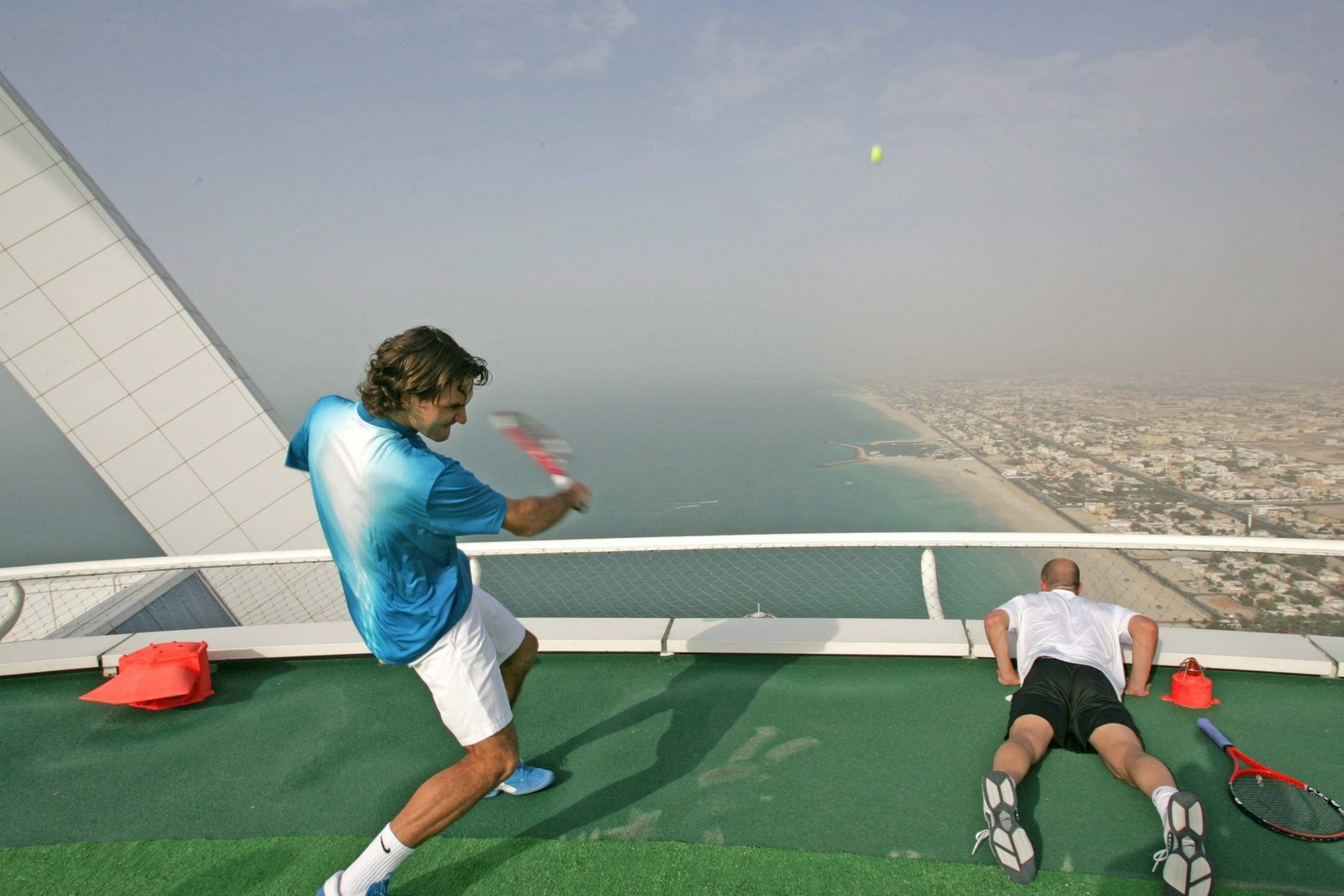 22 de febrero de 2005. El número uno del tenis mundial Roger Federer lanza una pelota al mar, mientras Andre Agassi  mira durante una sesión publicitaria en una pista de tenis única en el mundo, el Heliopuerto del hotel más lujoso del mundo, el Burj Al Arab.  Dubai, Emiratos Arabes Unidos. El heliopuerto del hotel, que está a 211 metros de altura, cubre una superficie de 415 metros cuadrados. EFE.