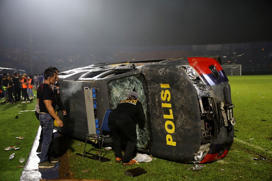 People stand next to a damaged car following a riot after the league BRI Liga 1 football match between Arema vs Persebaya at Kanjuruhan Stadium, Malang, East Java province, Indonesia, October 2, 2022, in this photo taken by Antara Foto. Antara Foto/H Prabowo/via REUTERS  ATTENTION EDITORS - THIS IMAGE HAS BEEN SUPPLIED BY A THIRD PARTY. MANDATORY CREDIT. INDONESIA OUT. NO COMMERCIAL OR EDITORIAL SALES IN INDONESIA.