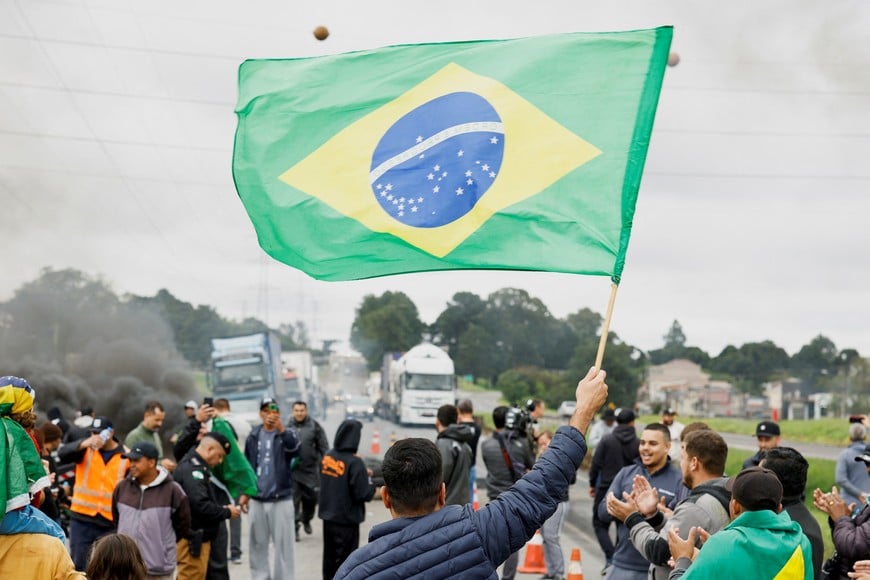 A man waves a Brazilian flag as supporters of Brazil's President Jair Bolsonaro, mainly truck drivers, block a highway during a protest over Bolsonaro's defeat in the presidential run-off election, in Curitiba, in the state of Parana, Brazil November 1, 2022. REUTERS/Rodolfo Buhrer