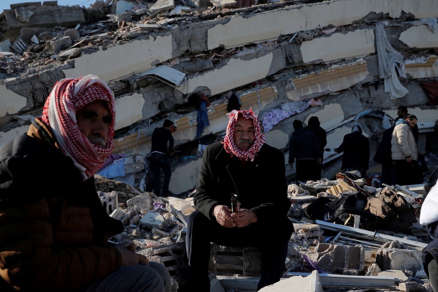 People sit in front of a collapsed building, following an earthquake in Kahramanmaras, Turkey February 7, 2023. REUTERS/Dilara Senkaya