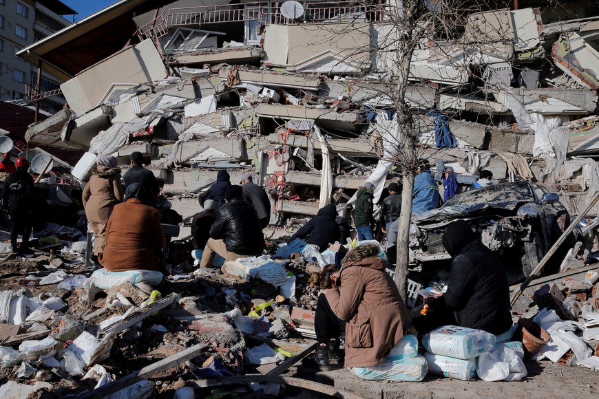 People sit in front of a collapsed building, following an earthquake in Kahramanmaras, Turkey February 7, 2023. REUTERS/Dilara Senkaya