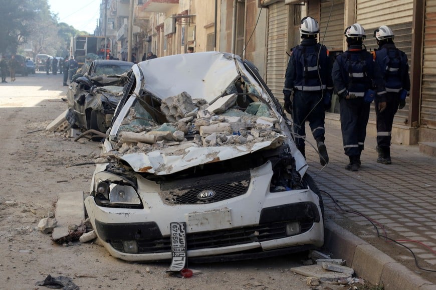 Rescuers walk past a damaged vehicle in the aftermath of an earthquake, in Jableh, Syria February 9, 2023. REUTERS/Yamam al Shaar
