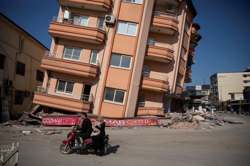 A man and a woman holding a baby ride past a destroyed building in the aftermath of the deadly earthquake in Kirikhan, Hatay province, Turkey, February 18, 2023. REUTERS/Eloisa Lopez