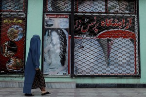 FILE PHOTO: A woman walks past a shop with defaced pictures of women in Kabul, Afghanistan October 6, 2021. REUTERS/Jorge Silva/File Photo