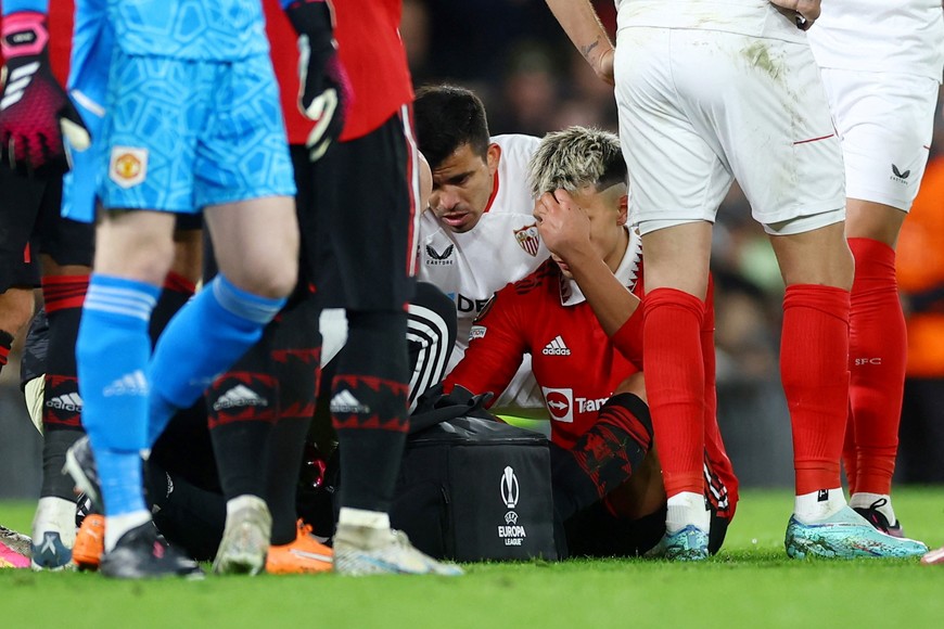 Soccer Football - Europa League - Quarter Final - First Leg - Manchester United v Sevilla - Old Trafford, Manchester, Britain - April 13, 2023 
Manchester United's Lisandro Martinez receives medical attention after sustaining an injury as Sevilla's Marcos Acuna looks on Action Images via Reuters/Lee Smith