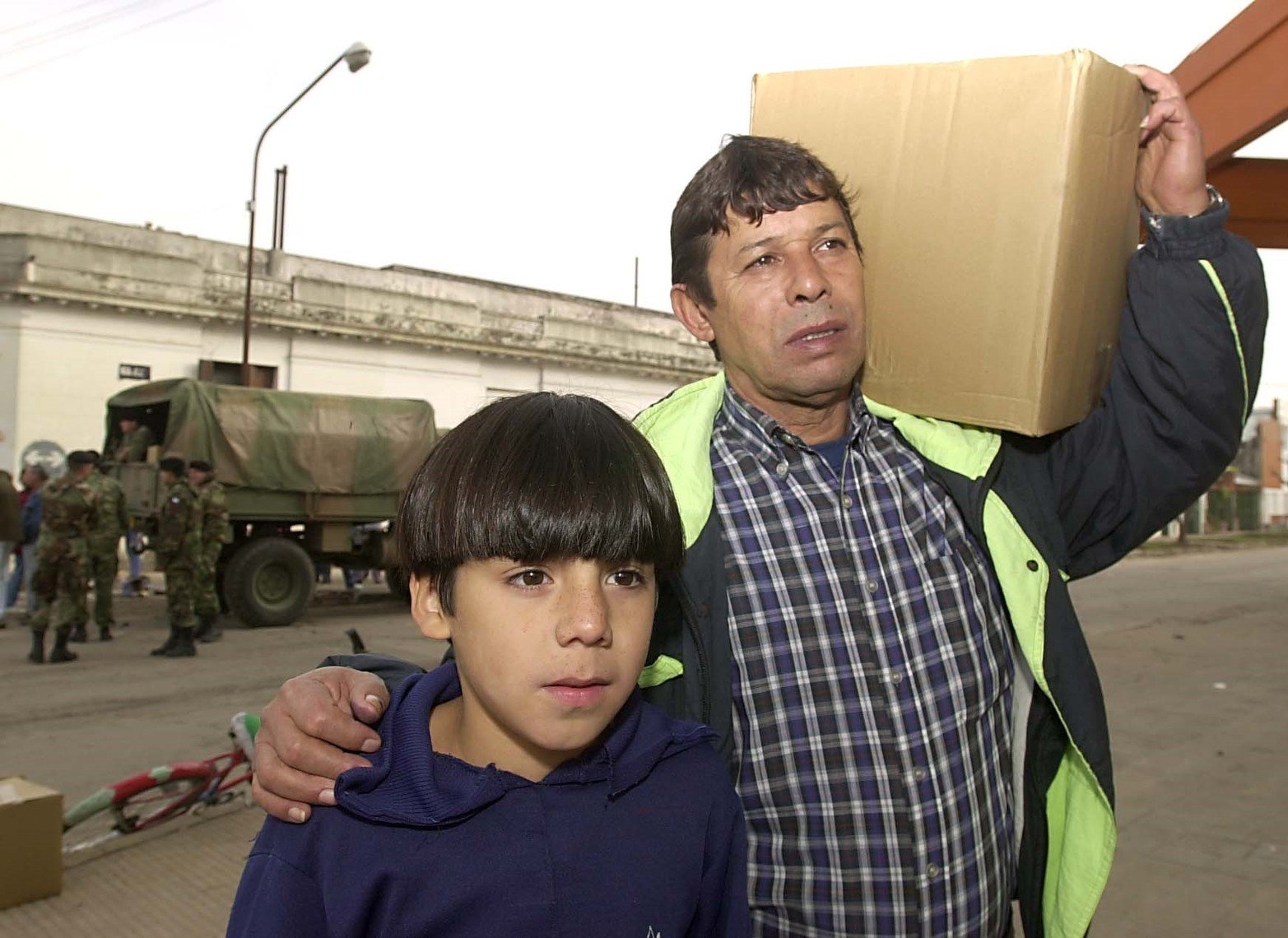 Un padre y un hijo se retiran luego de conseguir una caja de alimentos que repartió el Ejercito.
