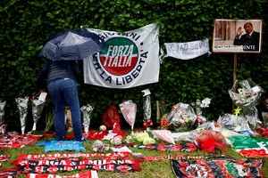 A person leaves a letter among flowers and football memorabilia near Villa San Martino, the residence of former Italian Prime Minister Silvio Berlusconi, to which his body was transported following his death, in Arcore near Milan, Italy, June 13, 2023. REUTERS/Yara Nardi