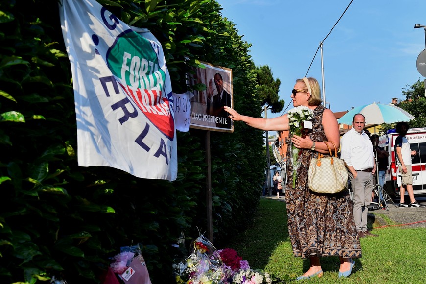 A woman touches a placard as people pay their respects outside former Italian Prime Minister Silvio Berlusconi's house, to which his body was transported following his death, in Arcore near Milan, Italy, June 12, 2023. REUTERS/Massimo Pinca