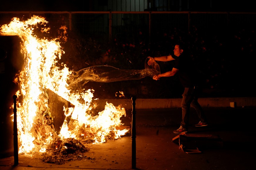 A person throws water to a burning container as people protest following the death of Nahel, a 17-year-old teenager killed by a French police officer in Nanterre during a traffic stop, and against police violence, in Paris, France, June 30, 2023. REUTERS/Juan Medina