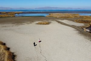 Gabriel Flores and Isabel Apaza walk on the dry cracked bed near the shore of Lake Titicaca in drought season in Huarina, Bolivia August 3, 2023. REUTERS/Claudia Morales