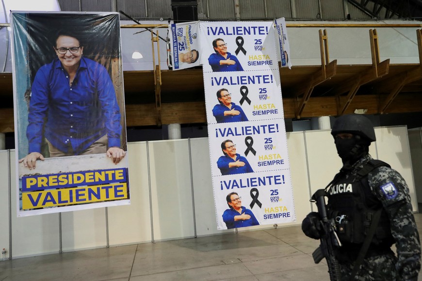 A police officer stands guard next to posters with images of Ecuadorean presidential candidate Fernando Villavicencio, a vocal critic of corruption and organized crime, during a post-mortem tribute at Quito Exhibition Center, after Villavicencio was killed during a campaign event, in Quito, Ecuador August 11, 2023.REUTERS/Henry Romero