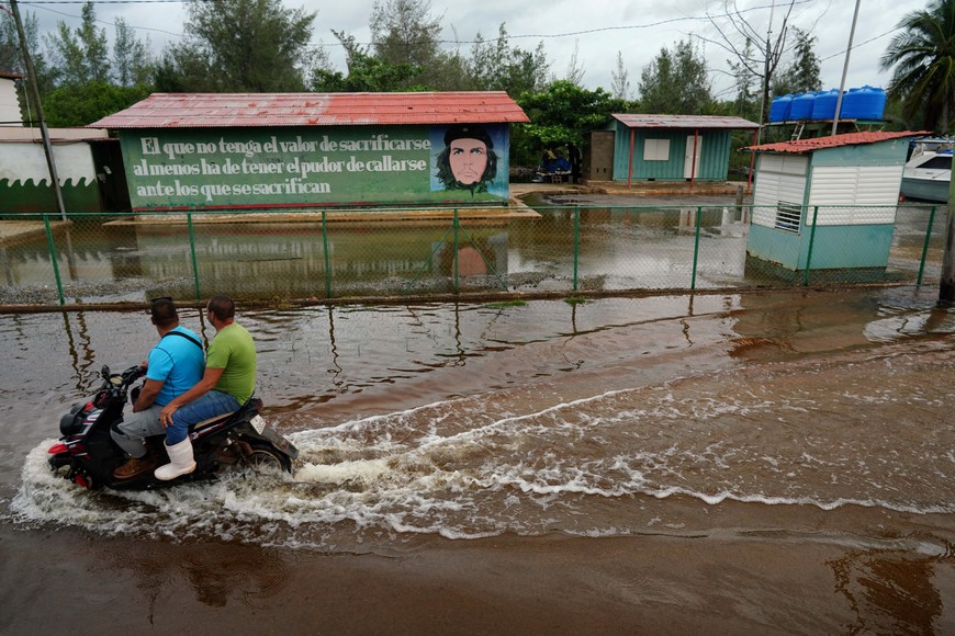 People on a flooded street pass by an image of late revolutionary hero Ernesto "Che" Guevara as Storm Idalia makes landfall in Cuba, in Guanimar, Cuba, August 28, 2023.  REUTERS/Alexandre Meneghini