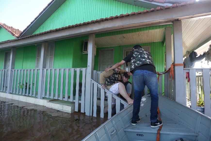 People assist a woman as she leaves her flooded house after a cyclone hit southern towns, in Venancio Aires, Rio Grande do Sul state, Brazil, September 5, 2023. REUTERS/Diego Vara