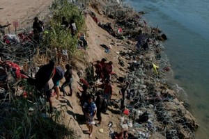 Miembros de la Guardia Nacional tratan de disuadir a los migrantes de trepar por el alambre de púas tras cruzar el Río Grande.