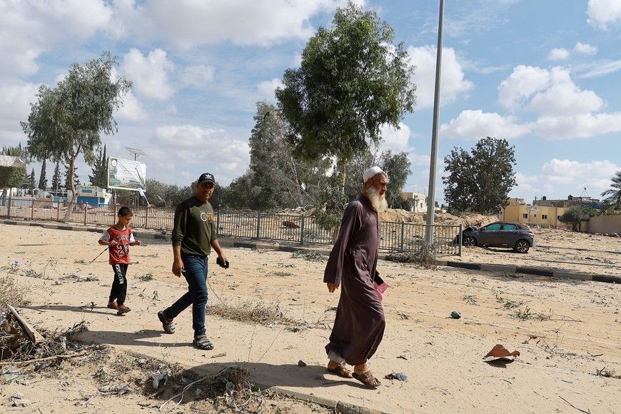 Palestinians walk near a damaged car, after Israeli strikes, in Rafah in the southern Gaza Strip October 17, 2023. REUTERS/Ibraheem Abu Mustafa