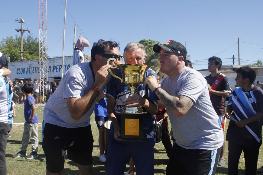 Gómez y Alarcón, del cuerpo técnico del campeón besan la copa junto a Norberto Tucho Monti, emblemático entrenador de la institución. El campeonato llevó su nombre. Foto: Nicolás Acosta.