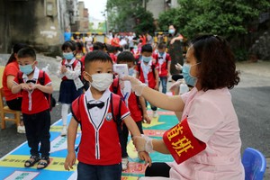 FILE PHOTO: A staff member takes body temperature measurement of schoolchildren at a kindergarten that has resumed operation following the coronavirus disease (COVID-19) outbreak, in Yongzhou, Hunan province, China May 11, 2020. Picture taken May 11, 2020. China Daily via REUTERS  ATTENTION EDITORS - THIS IMAGE WAS PROVIDED BY A THIRD PARTY. CHINA OUT./File Photo