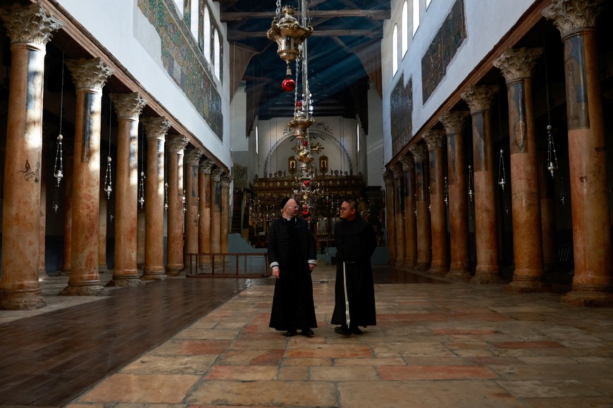 A priest and monk walk at the Church of the Nativity on the day of the launch of the beginning of the Christmas season, as the conflict between Israel and Palestinian Islamist group Hamas continues, in Bethlehem in the Israeli-occupied West Bank December 2, 2023. REUTERS/Ammar Awad
