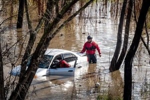 Trabajadores de búsqueda y rescate inspeccionan un automóvil alcanzado por una inundación generada por el aumento del caudal del río Guadalupe, en San José, California.