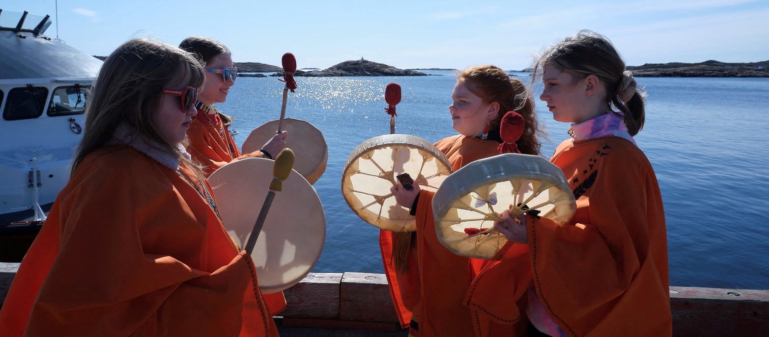 óvenes de la Primera Nación de Burgeo tocaron tambores durante un eclipse solar, con la Isla Eclipse vista al fondo, en Burgeo, Terranova, Canadá.