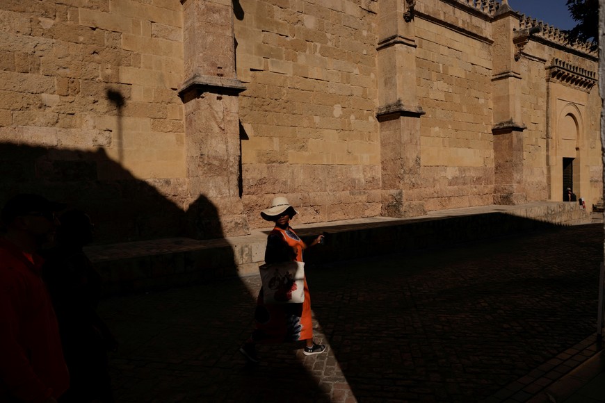 A tourist uses a hat to cover their head from the strong sun as they tour outside the Mosque of Cordoba, during a heat alert on a hot summer day, in downtown Cordoba, southern Spain, June 23, 2024. REUTERS/Jon Nazca