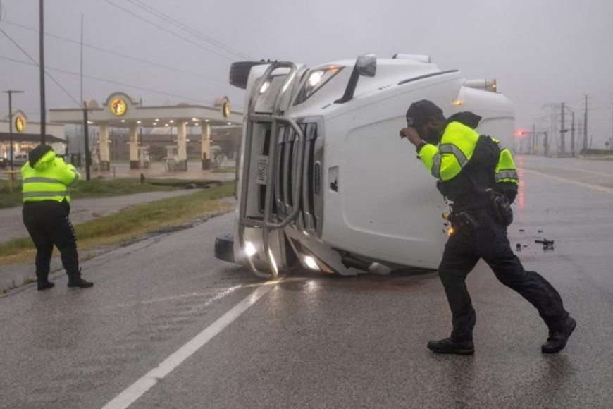 Agentes de policía luchan contra los fuertes vientos del huracán Beryl mientras buscan ocupantes en un camión semirremolque volcado en Freeport, Texas.