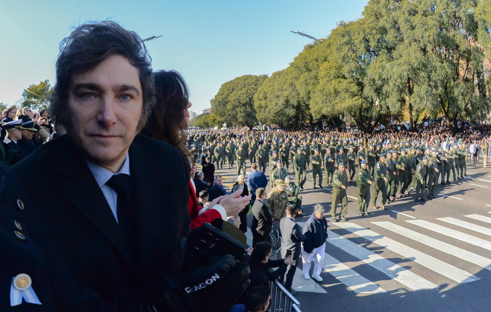 El Presidente Javier Milei posa para la foto con el desfile militar atrás.