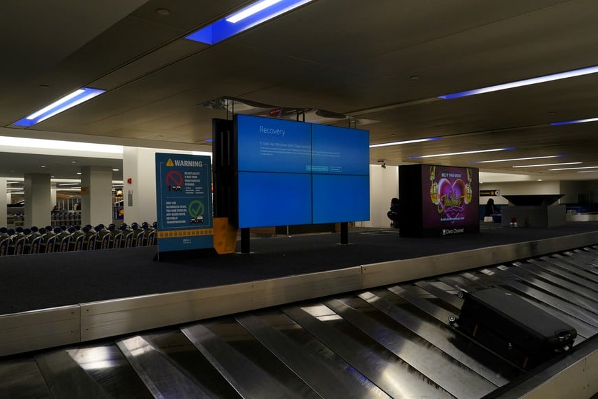 An item of checked luggage is seen near a monitor displaying a blue error screen, also known as the “Blue Screen of Death” at a baggage claim area inside Terminal C in Newark International Airport, after United Airlines and other airlines grounded flights due to a worldwide tech outage caused by an update to Crowdstrike's "Falcon Sensor" software which crashed Microsoft Windows systems, in Newark, New Jersey, U.S., July 19, 2024. REUTERS/Bing Guan