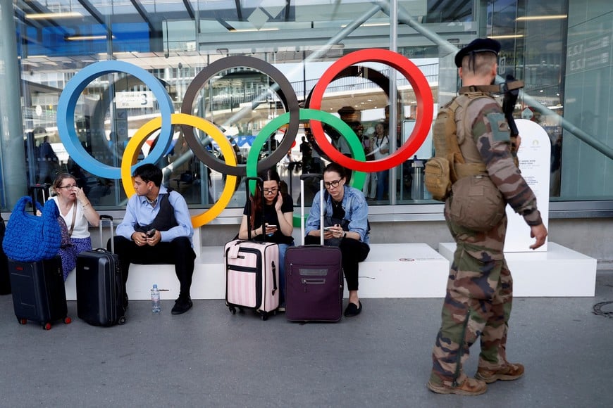 A French soldier walks past passengers sitting in front of the Olympic rings as they patrol outside the Terminal 3 at Orly Airport near Paris, ahead of the Paris 2024 Olympic and Paralympic Games, France July 19, 2024. REUTERS/Abdul Saboor