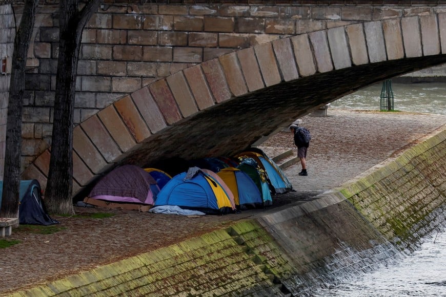A person stands near tents in which migrants live under the Pont d'Arcole bridge on the bank of the River Seine in Paris, France, March 25, 2024. REUTERS/Gonzalo Fuentes     TPX IMAGES OF THE DAY