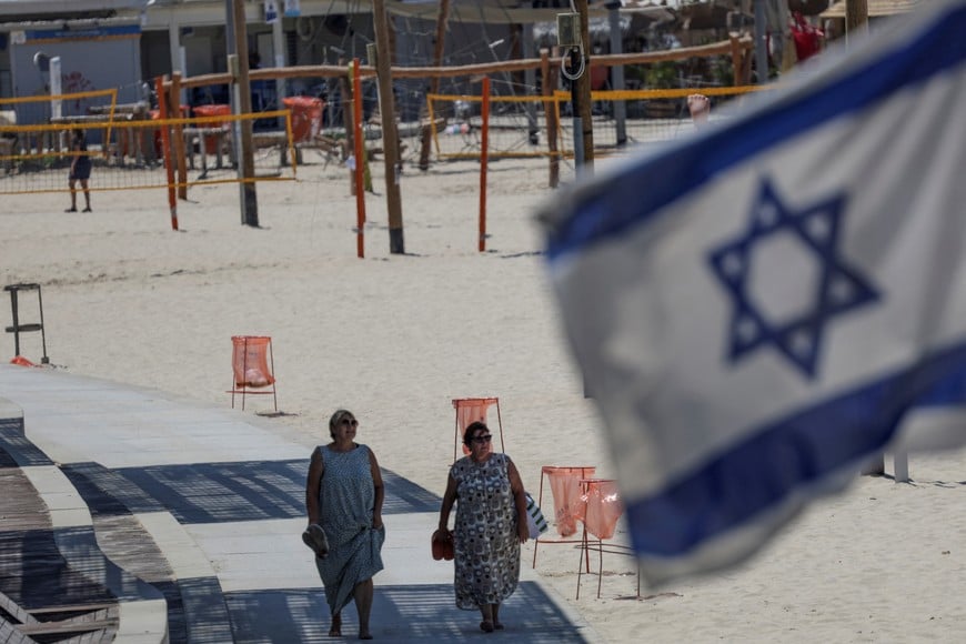 Women walk at the beach following announcements to vacate the area, after Hezbollah launched hundreds of rockets and drones towards Israel in what the Iranian-backed movement said was a response to the assassination of a senior commander in Beirut last month, in Tel Aviv, Israel, August 25, 2024. REUTERS/Florion Goga