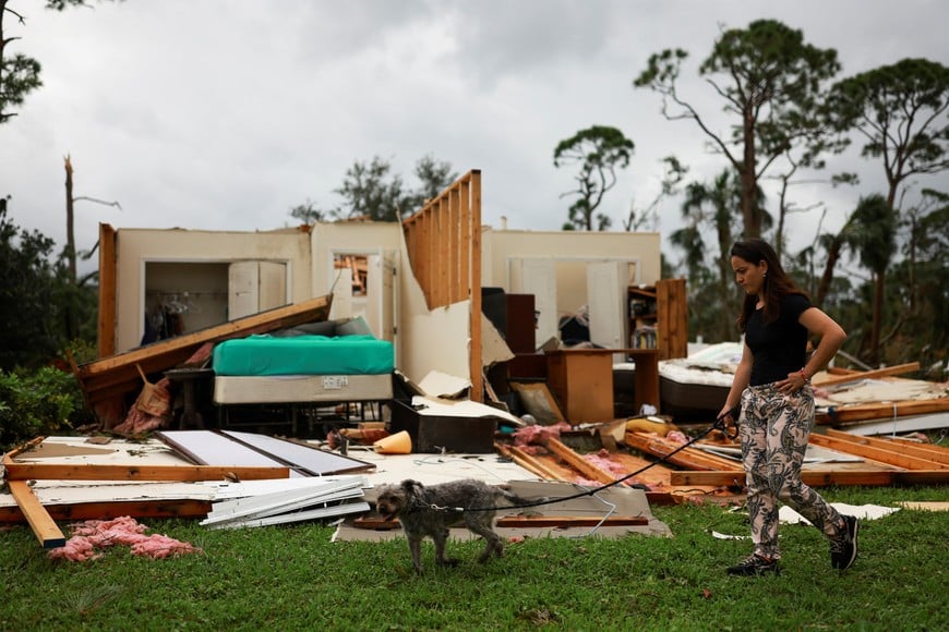 A woman walks a dog next to a damaged house following Hurricane Milton landfall, in Lakewood Park, near Fort Pierce, in St. Lucie County, Florida, U.S., October 11, 2024. REUTERS/Jose Luis Gonzalez