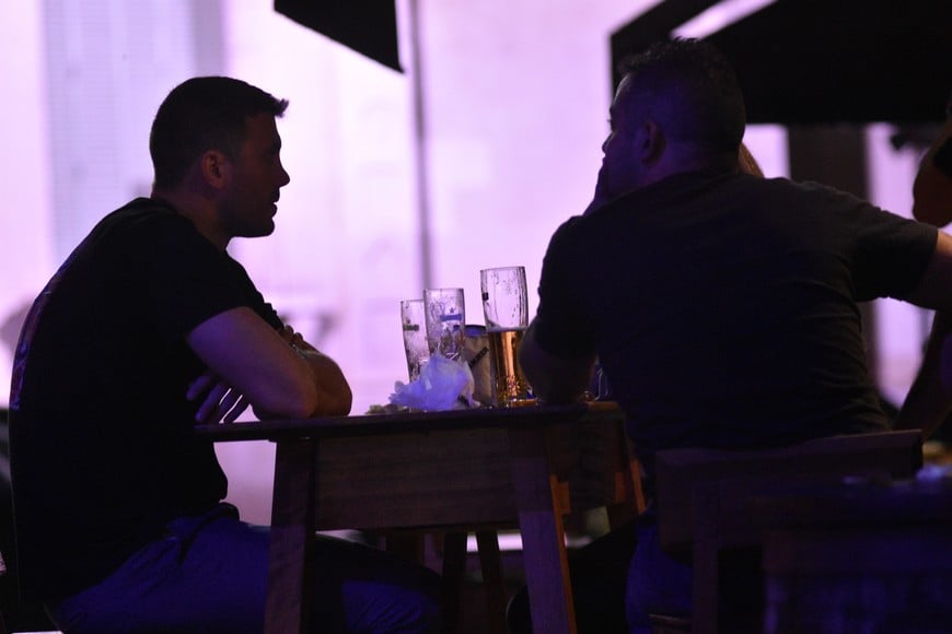 Dos amigos disfrutan de la noche en un bar. Los cuidacoches están en la esquina. Piden a la ciudadanía que denuncie.