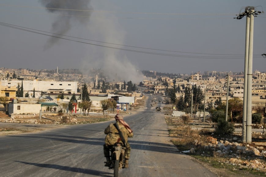 Smoke rises as a member of the rebels led by the Islamist militant group Hayat Tahrir al-Sham drives on a motorbike in al-Rashideen, Aleppo province, Syria November 29, 2024. REUTERS/Mahmoud Hasano