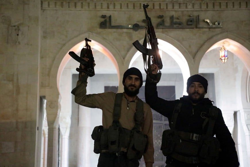 Rebel fighters hold weapons in front of Hama governor's building as they gather after Syrian rebels captured the city during their advance across northern Syria, in Hama, Syria December 5, 2024. REUTERS/Mahmoud Hassano