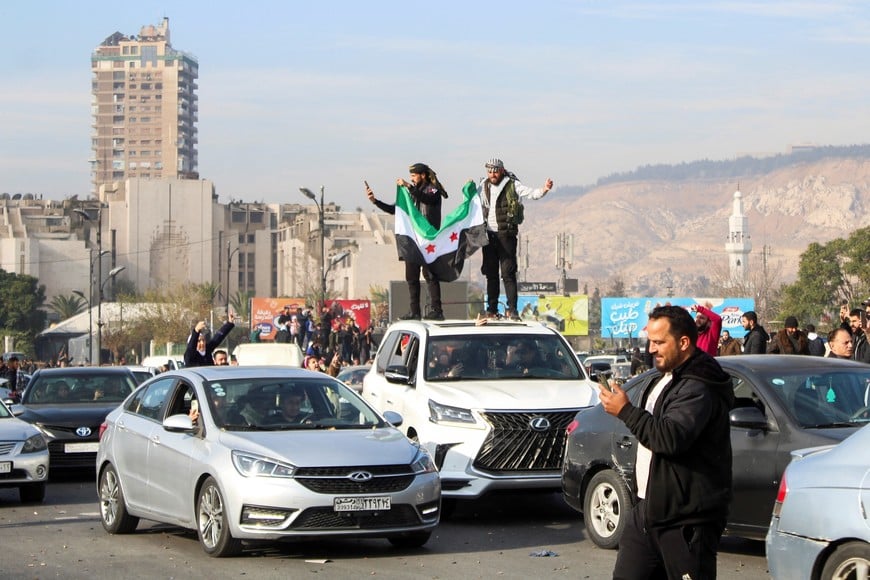 Men hold a Syrian opposition flag on the top of a vehicle as people celebrate after Syrian rebels announced that they have ousted President Bashar al-Assad,  in Damascus, Syria December 8, 2024. REUTERS/Firas Makdesi