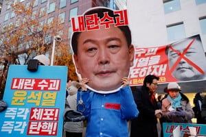 A protestor wears a cut-out of South Korean President Yoon Suk Yeol in a rally calling for his impeachment, who declared martial law, which was reversed hours later, near the National Assembly in Seoul, South Korea, December 8, 2024. REUTERS/Kim Soo-hyeon  REFILE - CORRECTING FROM "FACE MASK" TO "CUT-OUT".