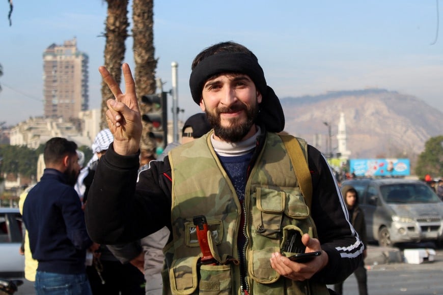 A rebel fighter shows victory sign as people celebrate after Syrian rebels announced that they have ousted President Bashar al-Assad, in Damascus, Syria December 8, 2024. REUTERS/Firas Makdesi