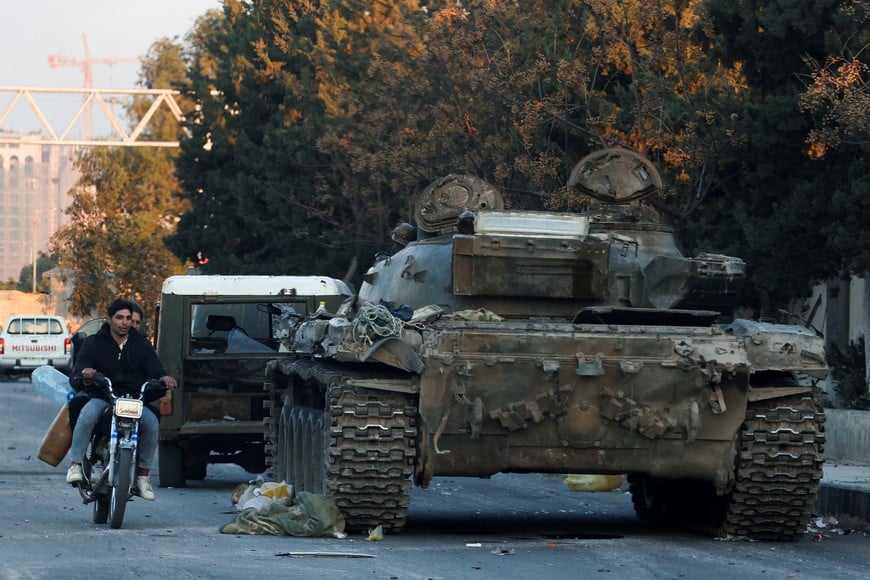 People on a bike ride past a tank that belonged to the Syrian Army, after Syrian rebels announced that they have ousted Syria's Bashar al-Assad, in Damascus, Syria, December 8, 2024. REUTERS/Mohamed Azakir