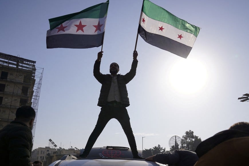 A man holds Syrian opposition flags as he celebrates after Syria's army command notified officers on Sunday that President Bashar al-Assad's 24-year authoritarian rule has ended, a Syrian officer who was informed of the move told Reuters, following a rapid rebel offensive that took the world by surprise, in Aleppo, Syria December 8, 2024. REUTERS/Karam al-Masri