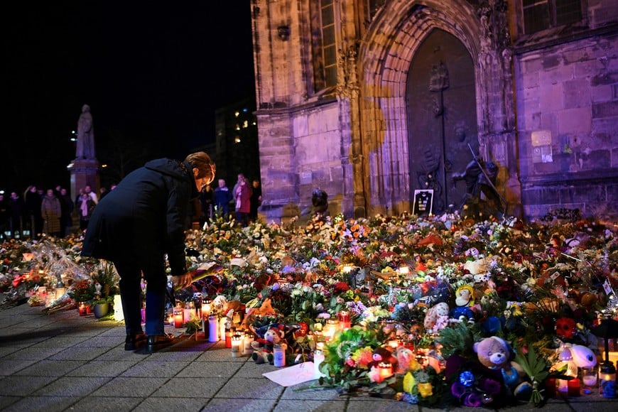 A woman bends to place a tribute with flowers and candles left near the 'Alter Markt' Christmas market, where a man drove a car into the crowd through an emergency exit route on Friday evening, in Magdeburg, Germany, December 22, 2024.  REUTERS/Annegret Hilse