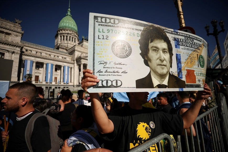 A supporter of Argentina's President-elect Javier Milei holds up a representation of a 100 dollar bill featuring an image of Javier Milei, on the day of his swearing-in ceremony, outside the National Congress, in Buenos Aires, Argentina December 10, 2023. REUTERS/Agustin Marcarian