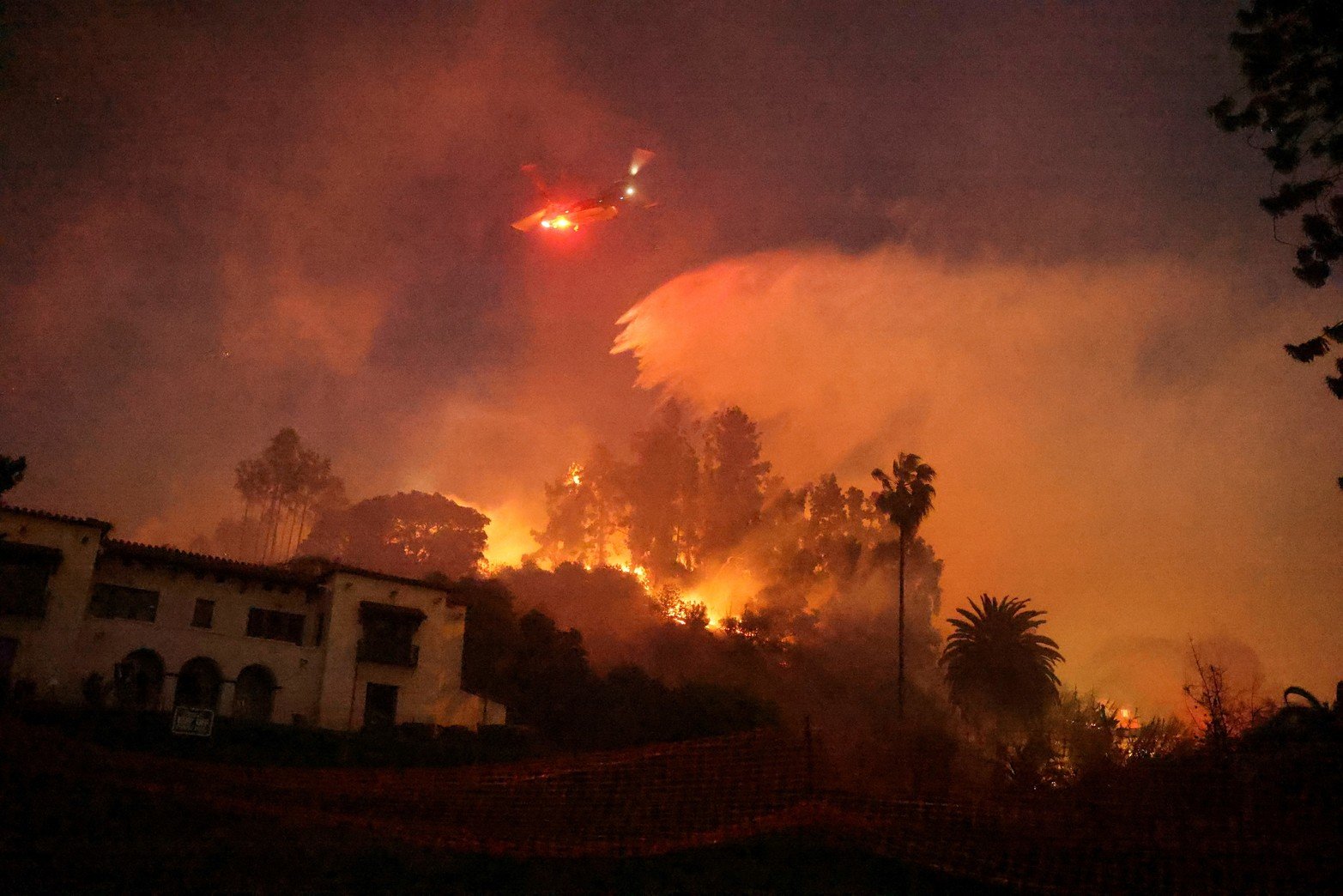 Un helicóptero realiza una caída de agua, mientras el humo y las llamas se elevan . Créditos: David Swanson