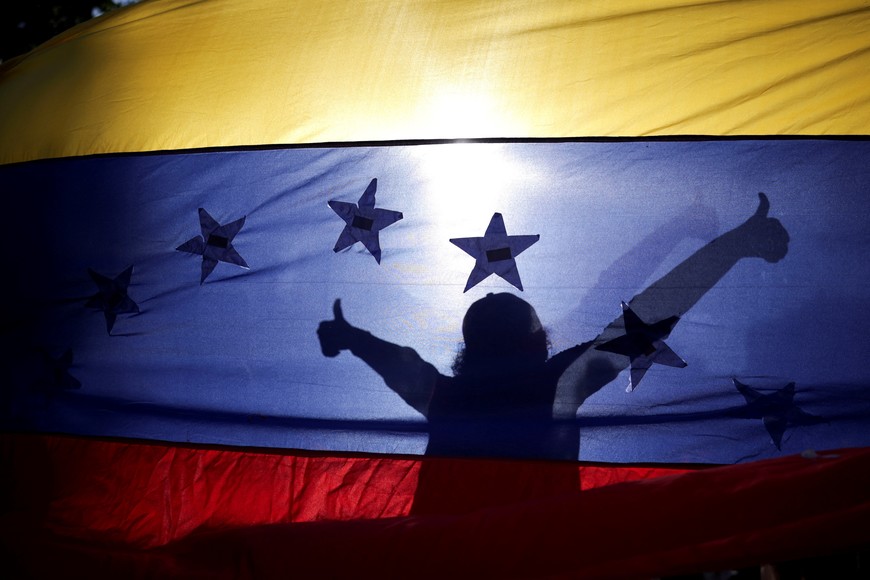 A Venezuelan opposition supporter is silhouetted against a Venezuela's flag during a protest ahead of the Friday inauguration of President Nicolas Maduro for his third term, in Santiago, Chile January 9, 2025. REUTERS/Pablo Sanhueza