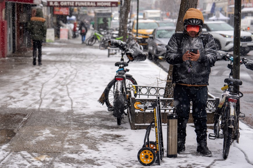 A delivery worker looks at his phone during a snowfall in the Harlem Section of New York City, U.S., January 6, 2025. REUTERS/David Dee Delgado