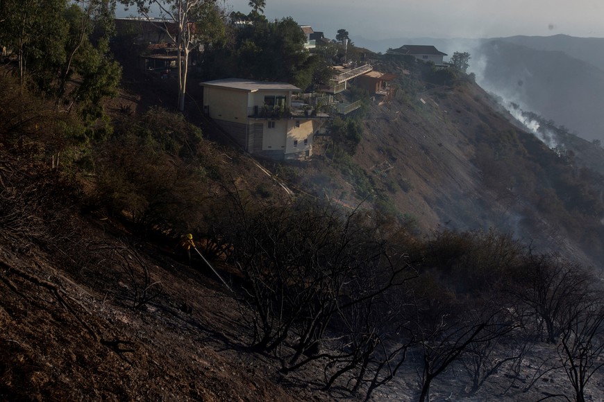 A firefighter extinguishes a hot spot as the Palisades Fire, one of several simultaneous blazes that have ripped across Los Angeles County, burns in Mandeville Canyon, a neighborhood of Los Angeles, California, U.S., January 11, 2025. REUTERS/Ringo Chiu