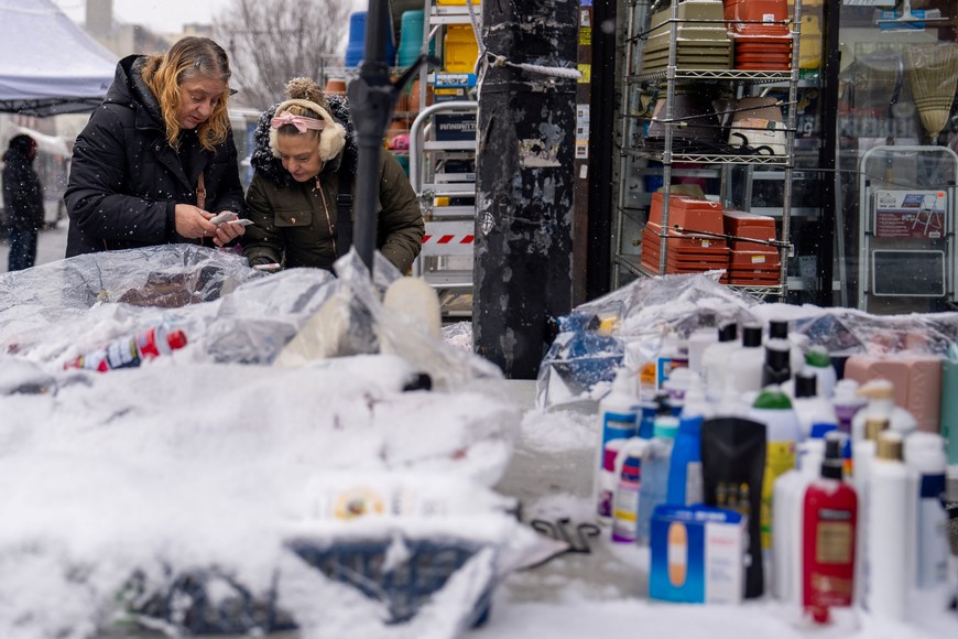 Two people look at items for sale at a street vendors table during a snowfall in the Harlem Section of New York City, U.S., January 6, 2025. REUTERS/David Dee Delgado