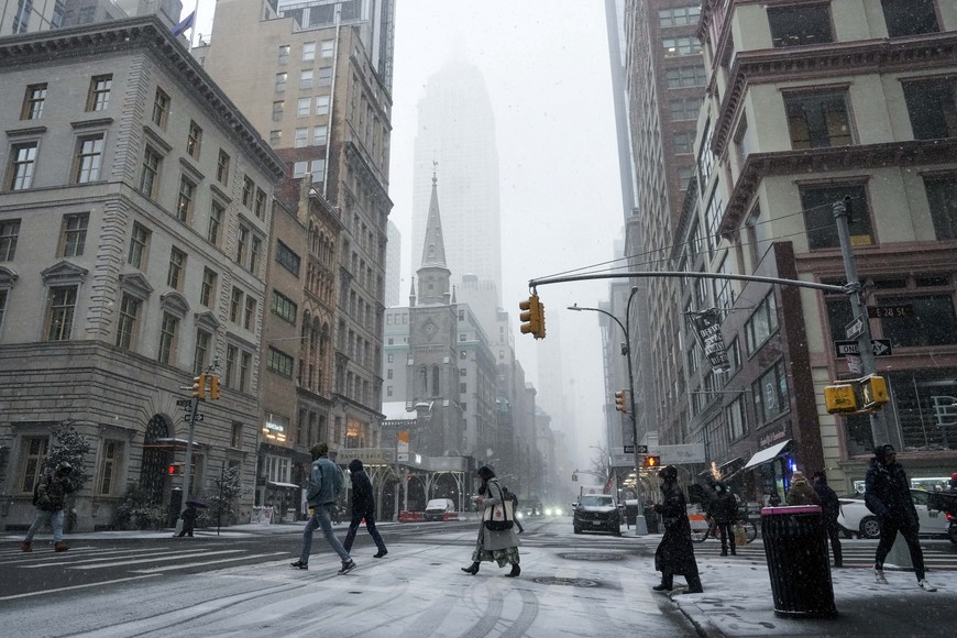 People cross the street, with the Empire State Building behind, during snowfall in New York City, U.S., January 6, 2025. REUTERS/Adam Gray