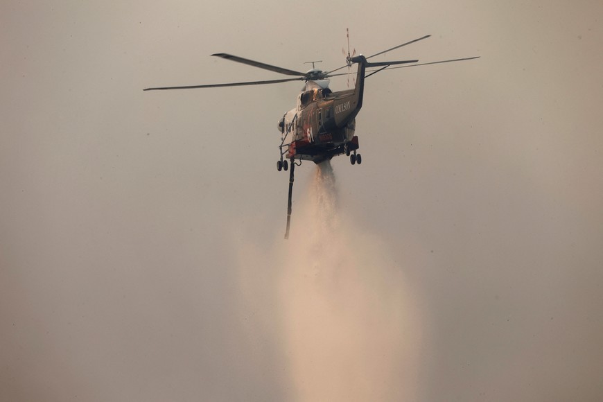 A helicopter drops water on the Palisades Fire, one of simultaneous blazes that have ripped across Los Angeles County, along Mandeville Canyon, in the Encino neighborhood of Los Angeles, California, U.S., January 11, 2025. REUTERS/Daniel Dreifuss